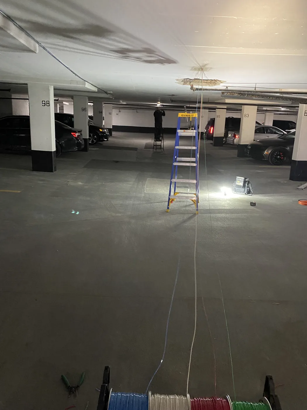 Electrician on a ladder pulling new circuit wiring in an underground parking garage of a managed Toronto building