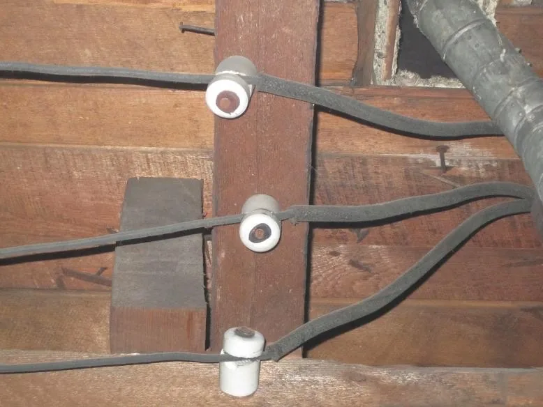Close-up of knob-and-tube wiring with ceramic knobs on a wooden joist